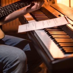 man playing acoustic guitar and piano close-up, recording notes, beautiful color background, music activity concept
